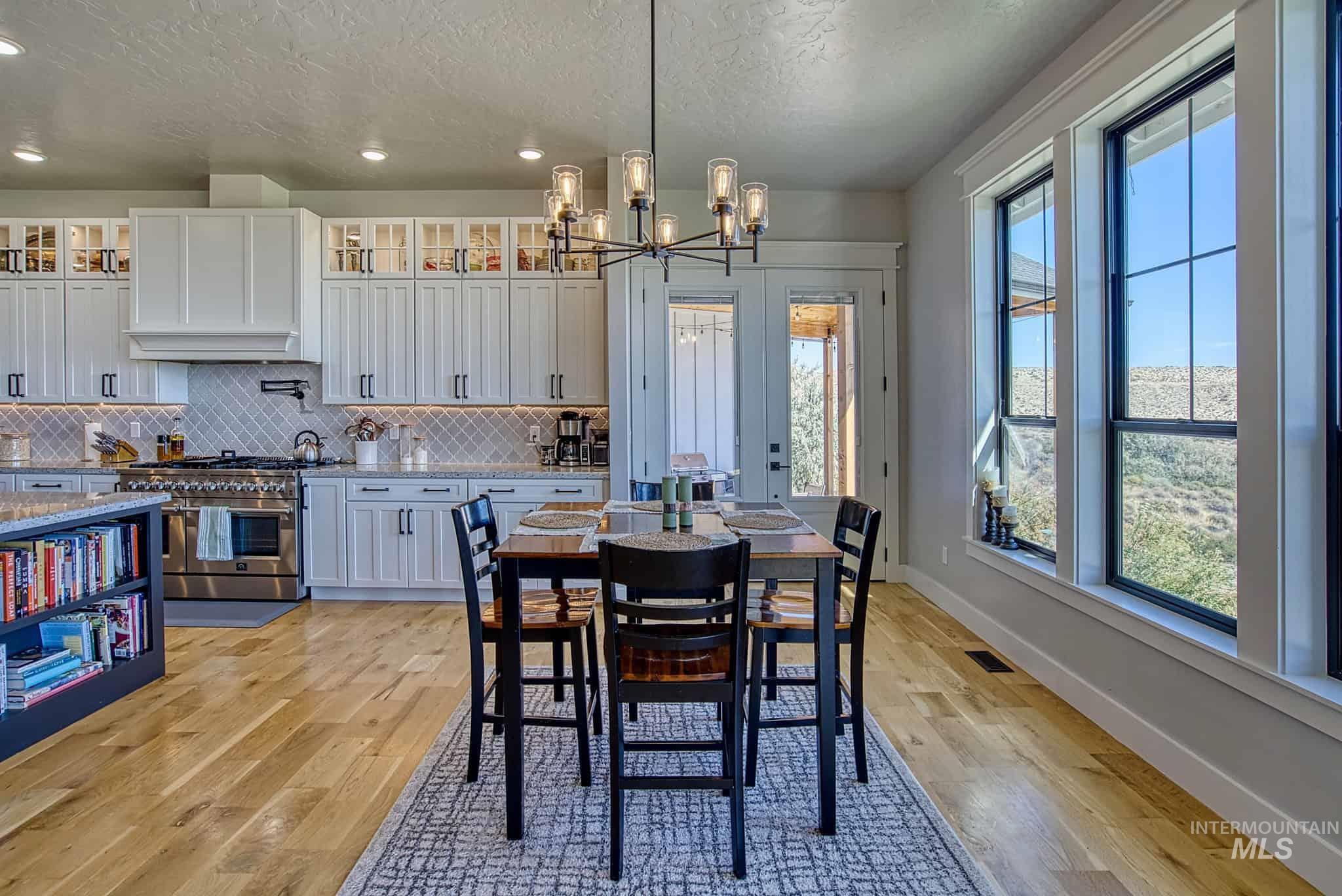 876 Coyote Gulch Road Adrian, OR 97901 - Photo 5 of 50 White shaker cabinetry, wood-finish flooring, black-framed windows, stainless steel range, and a modern chandelier