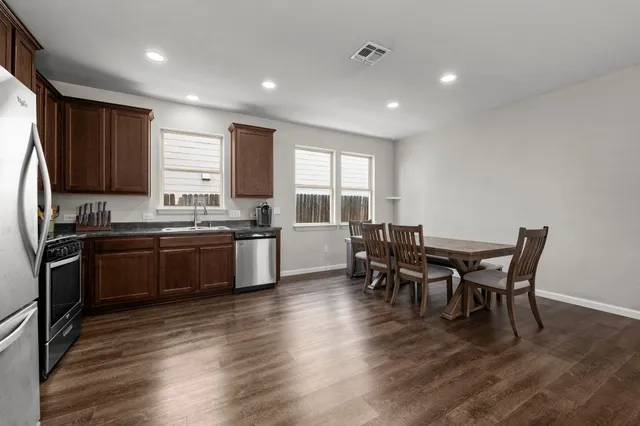 a kitchen with granite countertop a refrigerator a stove a sink a dining table and chairs