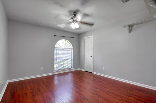 an empty room with wooden floor chandelier fan and windows