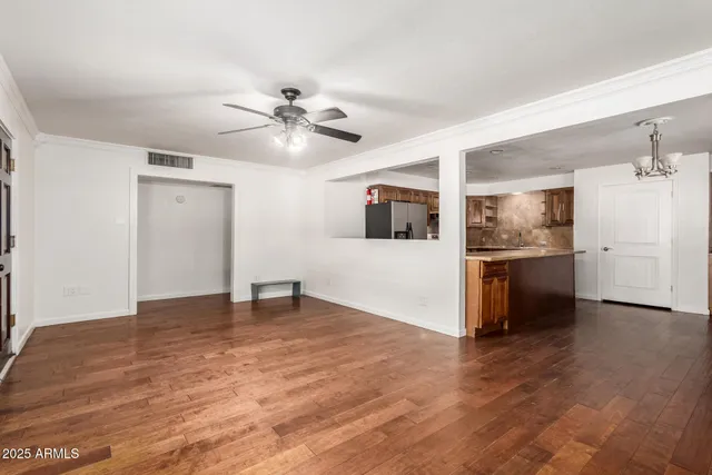 a view of an empty room with chandelier fan and wooden floor