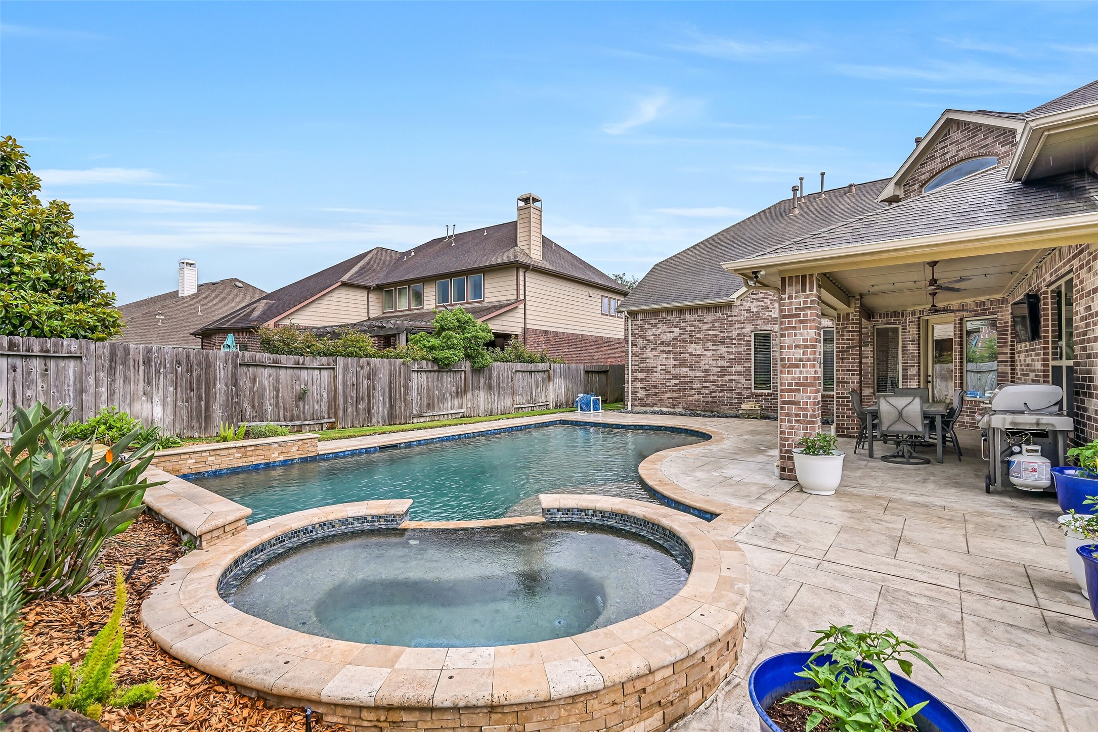 1008 Point Isabel Lane Friendswood, TX 77546 - Photo 49 of 50 A closer look at the raised spa highlights the pebble-tec finish, tanning ledge with bubbler, attractive stone coping, and integrated design, offering a comfortable space to relax while enjoying the surrounding backyard setting.