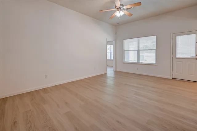 an empty room with wooden floor fan and windows
