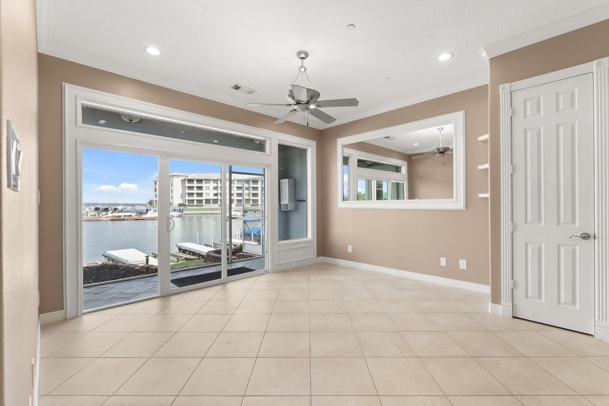 168 Lake Point Boulevard, Unit C102 Conroe, TX 77356 - Photo 2 of 35 Bright, open room with large windows and sliding doors offering stunning waterfront views. Features tiled flooring, a ceiling fan, and a large wall mirror, creating a spacious and airy feel.