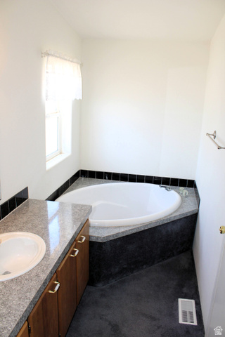 22580 Spring Creek Drive, Unit B61 Fairview, UT 84629 - Photo 23 of 39 Bathroom featuring a built-in soaking tub with a granite surround, a vanity with a granite countertop and integrated sink, wood-finish cabinetry, and dark flooring