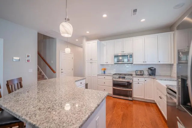 a kitchen with kitchen island a stove a sink a refrigerator and white cabinets with wooden floor