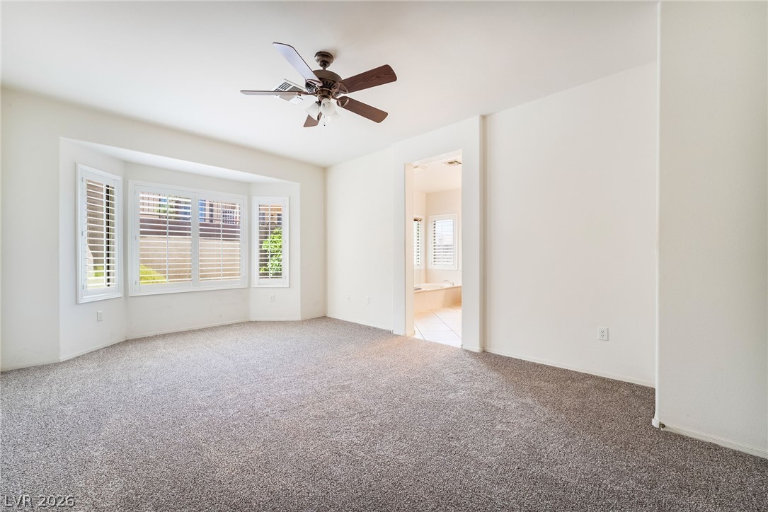 3033 Hartsville Road Henderson, NV 89052 - Photo 25 of 41 A spacious primary bedroom with bay windows, carpeted floors, and private bath access.