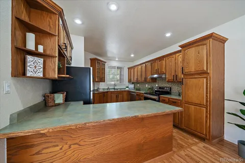 a large kitchen with stainless steel appliances granite countertop a refrigerator a oven and a sink with wooden cabinets