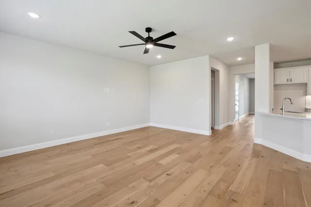 a view of an empty room with wooden floor and a ceiling fan
