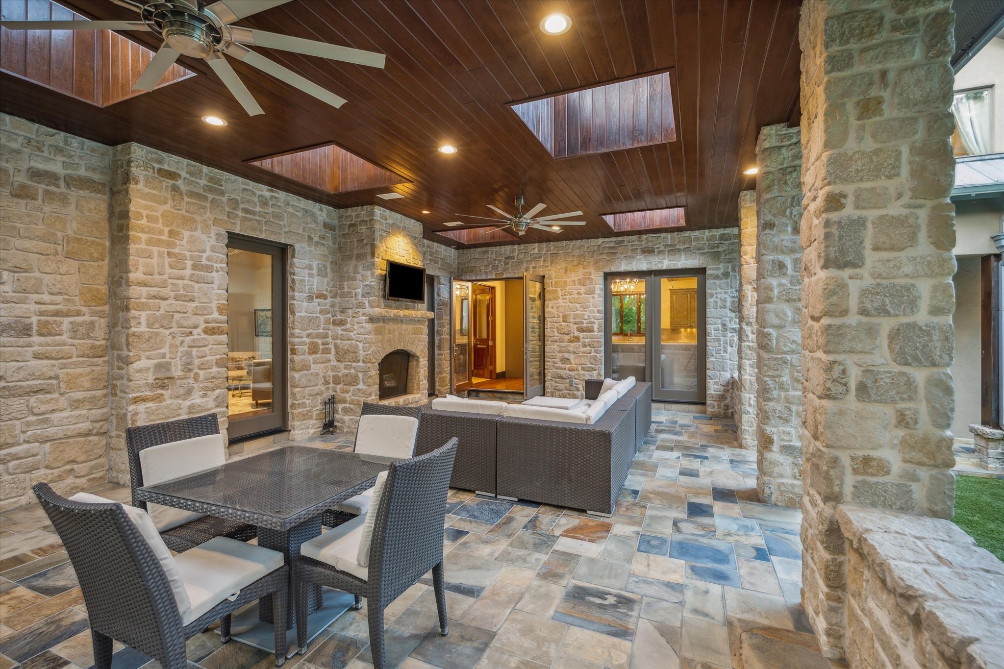 354 Piney Point Road Houston, TX 77024 - Photo 41 of 50 Step outside onto your kitchen deck overlooking the saltwater pool, featuring a built-in gas fireplace set against a stunning stone accent wall. The space boasts slate tile flooring, a picturesque wood ceiling with recessed lighting, and multiple skylights, creating a bright and inviting outdoor area that is both covered and protected.