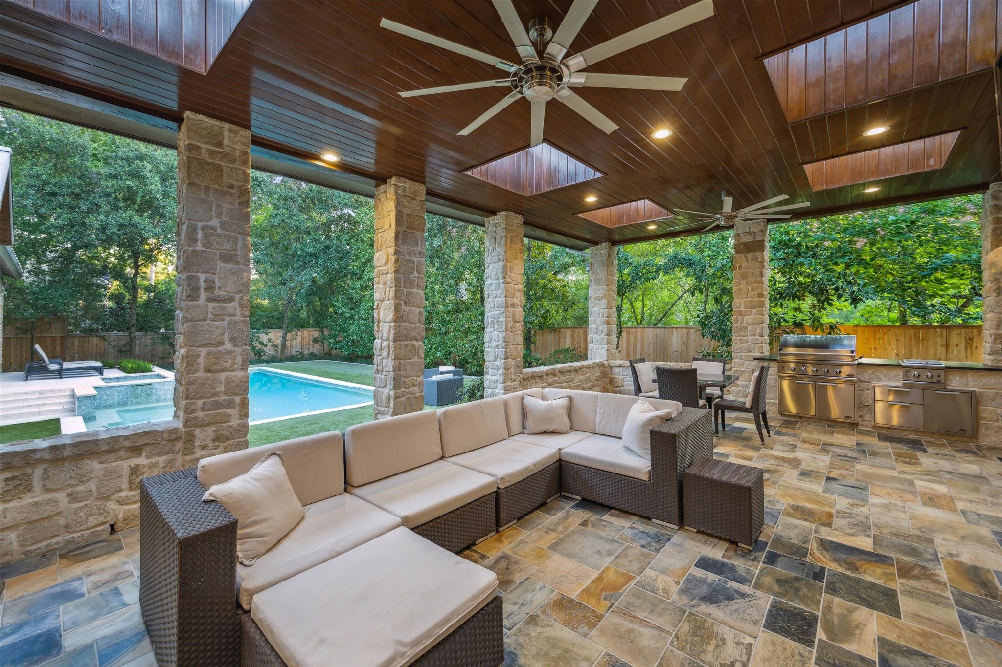 354 Piney Point Road Houston, TX 77024 - Photo 42 of 50 Step outside onto your kitchen deck overlooking the saltwater pool, featuring a built-in gas fireplace set against a stunning stone accent wall. The space boasts slate tile flooring, a picturesque wood ceiling with recessed lighting, and multiple skylights, creating a bright and inviting outdoor area that is both covered and protected.