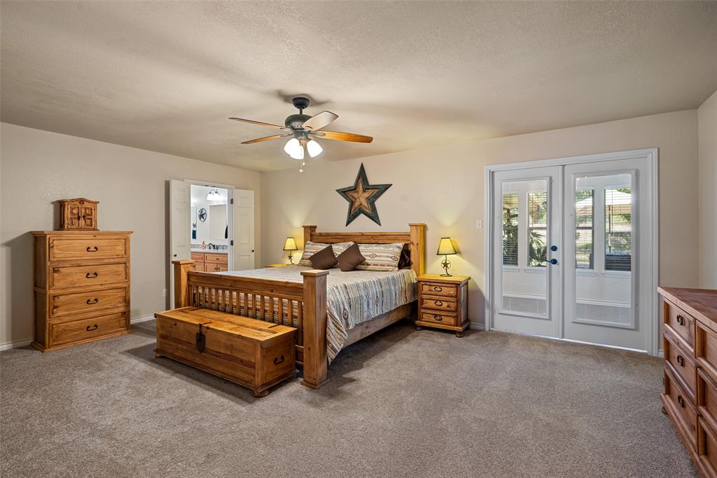 10517 Ravenswood Road Granbury, TX 76049 - Photo 18 of 35 a spacious bedroom with a bed a chandelier and a dresser