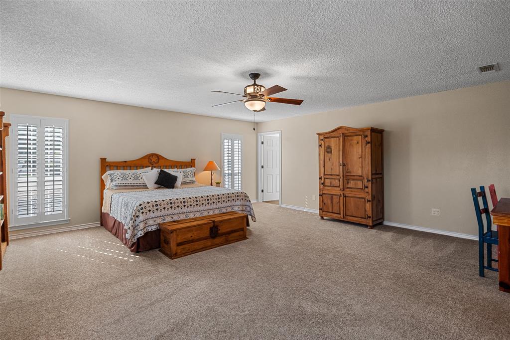 10517 Ravenswood Road Granbury, TX 76049 - Photo 22 of 35 a spacious bedroom with a bed and a chandelier