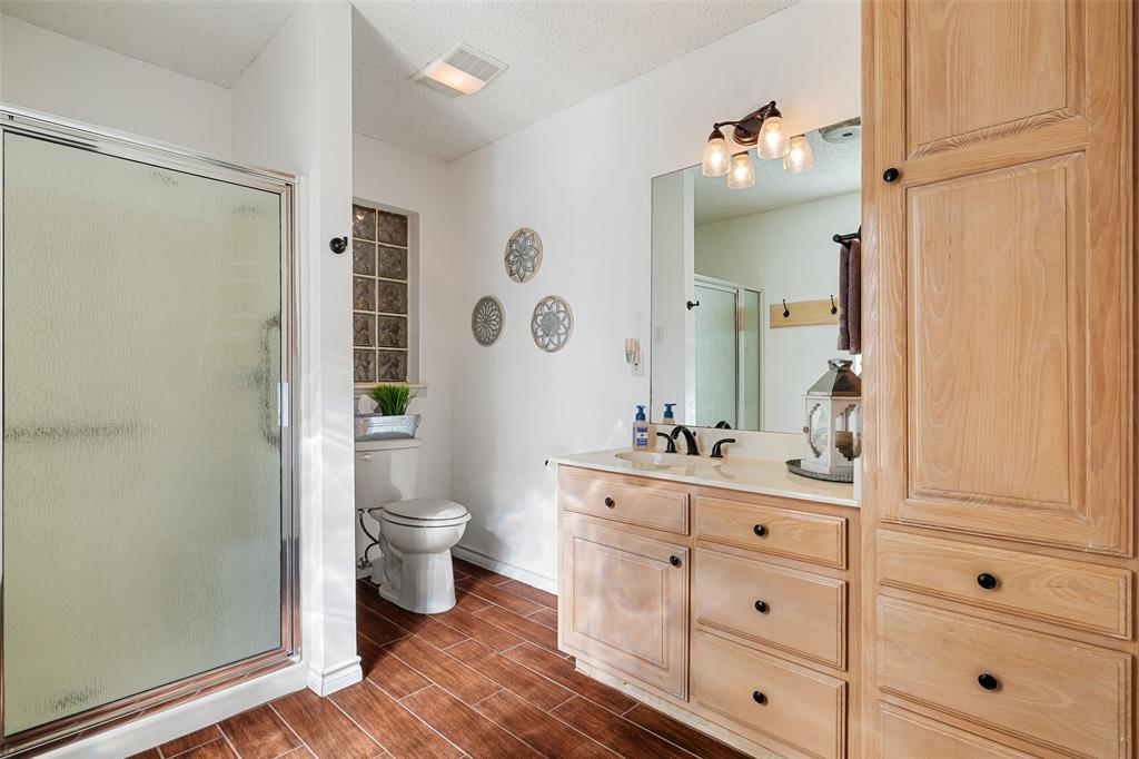 10517 Ravenswood Road Granbury, TX 76049 - Photo 24 of 35 a bathroom with a toilet a sink a glass door a shower and a mirror