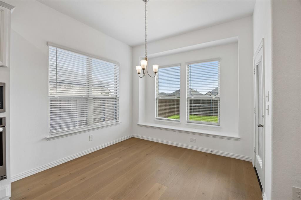 1303 Wheelwright Drive Forney, TX 75126 - Photo 18 of 39 Bright dining area with wood-finish flooring, a contemporary chandelier, multiple windows with blinds, a window seat, and a paneled door