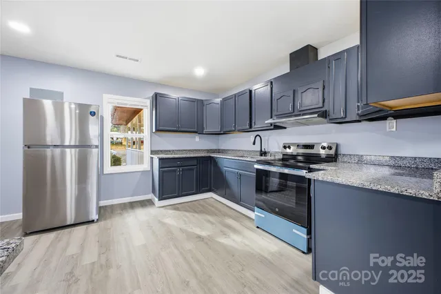 a kitchen with stainless steel appliances granite countertop a refrigerator a sink dishwasher a stove top oven a refrigerator and cabinets with wooden floor