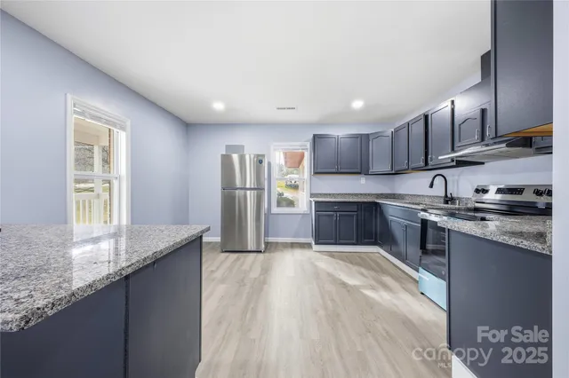 a kitchen with stainless steel appliances granite countertop a sink a stove a refrigerator cabinets and a window