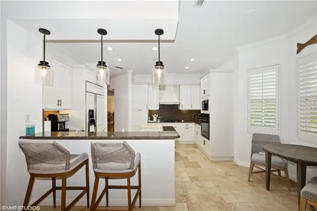 a kitchen with kitchen island granite countertop a dining table chairs and white cabinets