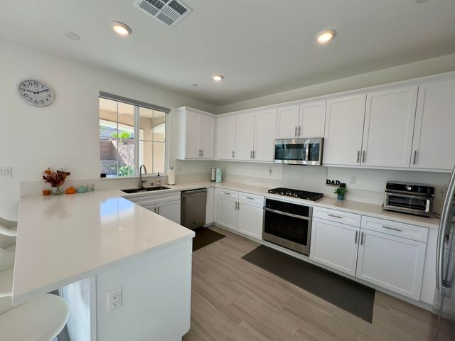 a kitchen with stainless steel appliances white cabinets a sink dishwasher a stove and a refrigerator with wooden floor