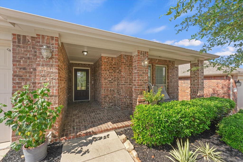 409 Harding Lane Lavon, TX 75166 - Photo 2 of 34 Brick exterior featuring a covered front porch with brick flooring, a dark entry door with glass paneling, and an exterior wall lantern