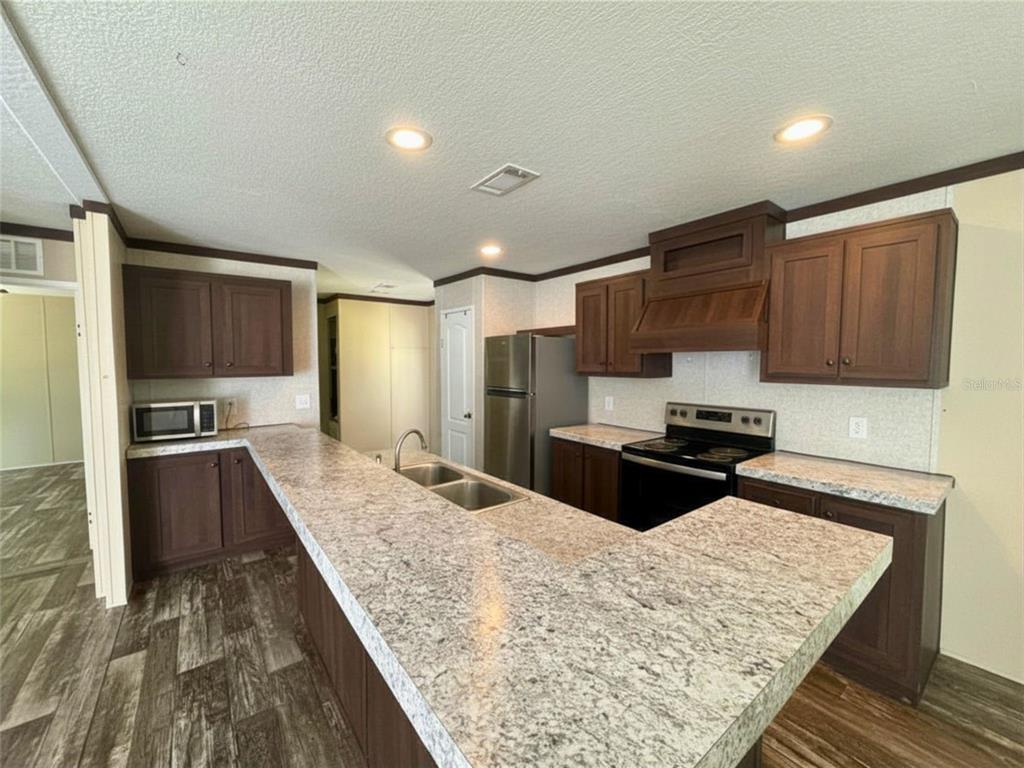 9827 Southeast Hoth Road Arcadia, FL 34266 - Photo 26 of 28 a kitchen with stainless steel appliances kitchen island granite countertop a refrigerator oven a sink dishwasher and wooden cabinets with wooden floor
