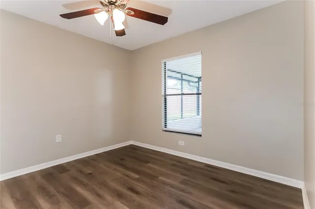 an empty room with wooden floor chandelier fan and windows