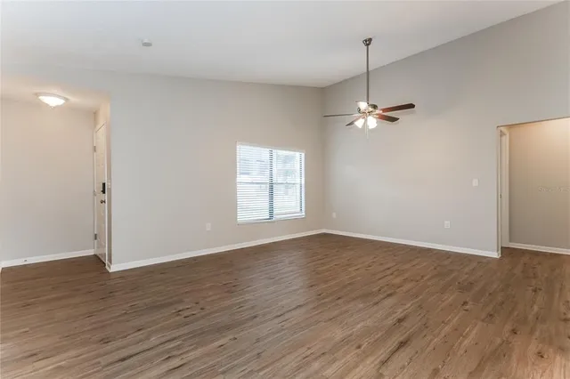 an empty room with wooden floor fan and windows