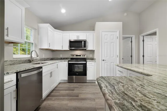 a kitchen with granite countertop a stove top oven a sink dishwasher and a refrigerator with wooden floor