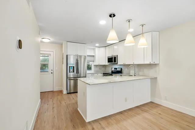 a kitchen with stainless steel appliances a refrigerator a sink dishwasher a stove and white cabinets with wooden floor