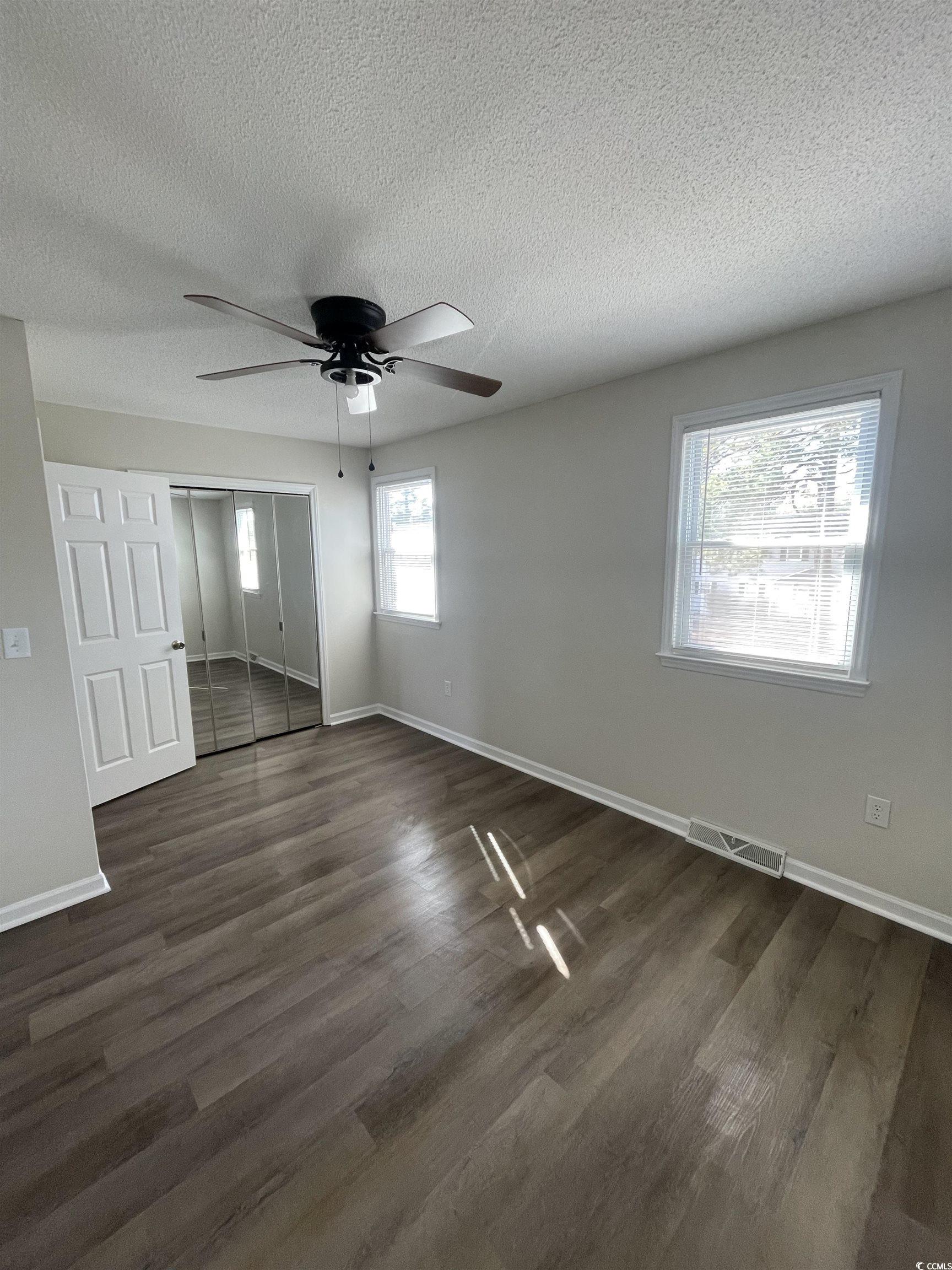4641 Socastee Boulevard, Unit E1 Myrtle Beach, SC 29588 - Photo 4 of 20 Unfurnished bedroom featuring dark wood finished floors, a textured ceiling, a closet, and a ceiling fan