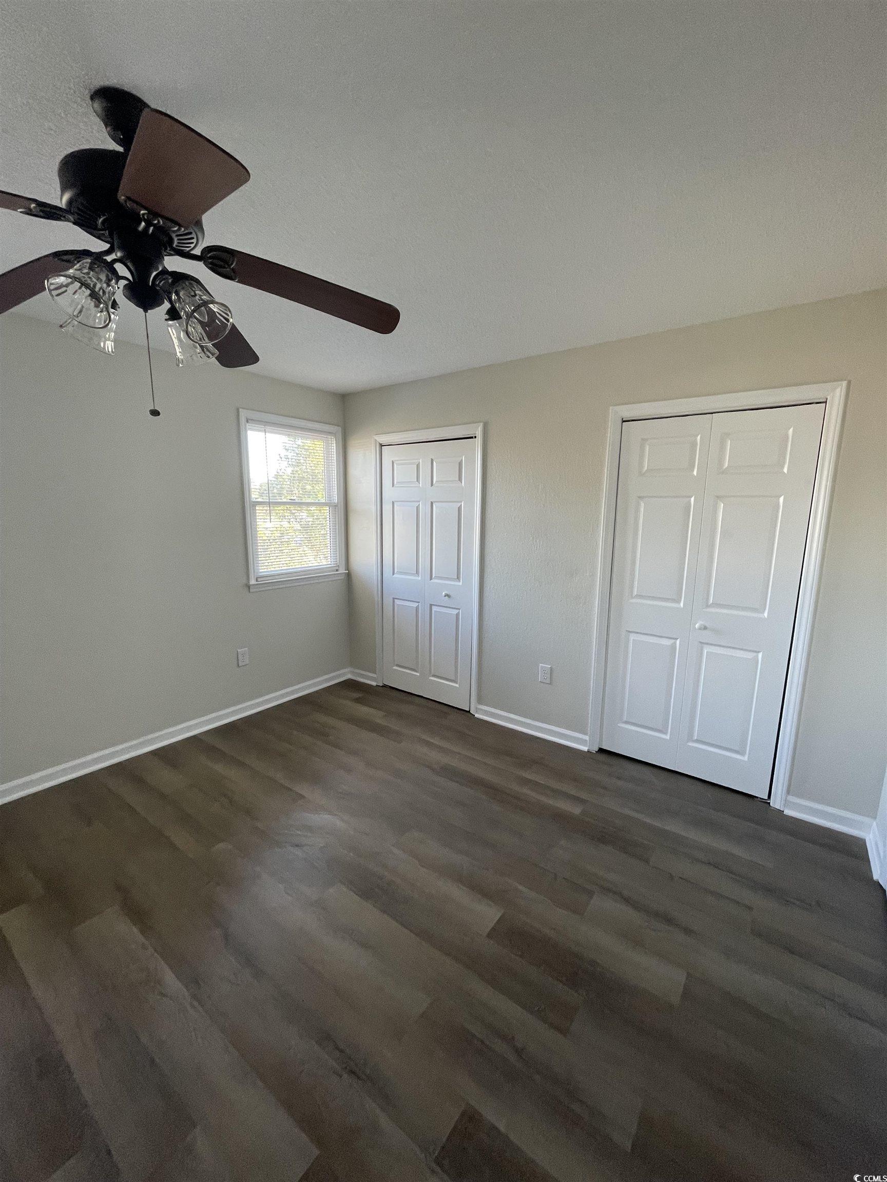 4641 Socastee Boulevard, Unit E1 Myrtle Beach, SC 29588 - Photo 9 of 20 Unfurnished bedroom featuring multiple closets, dark wood finished floors, and a ceiling fan