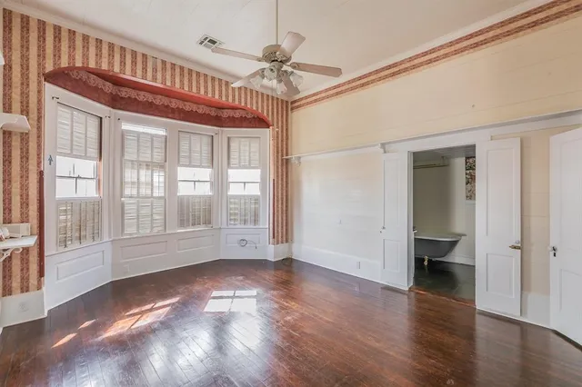 a view of an empty room with wooden floor and a ceiling fan