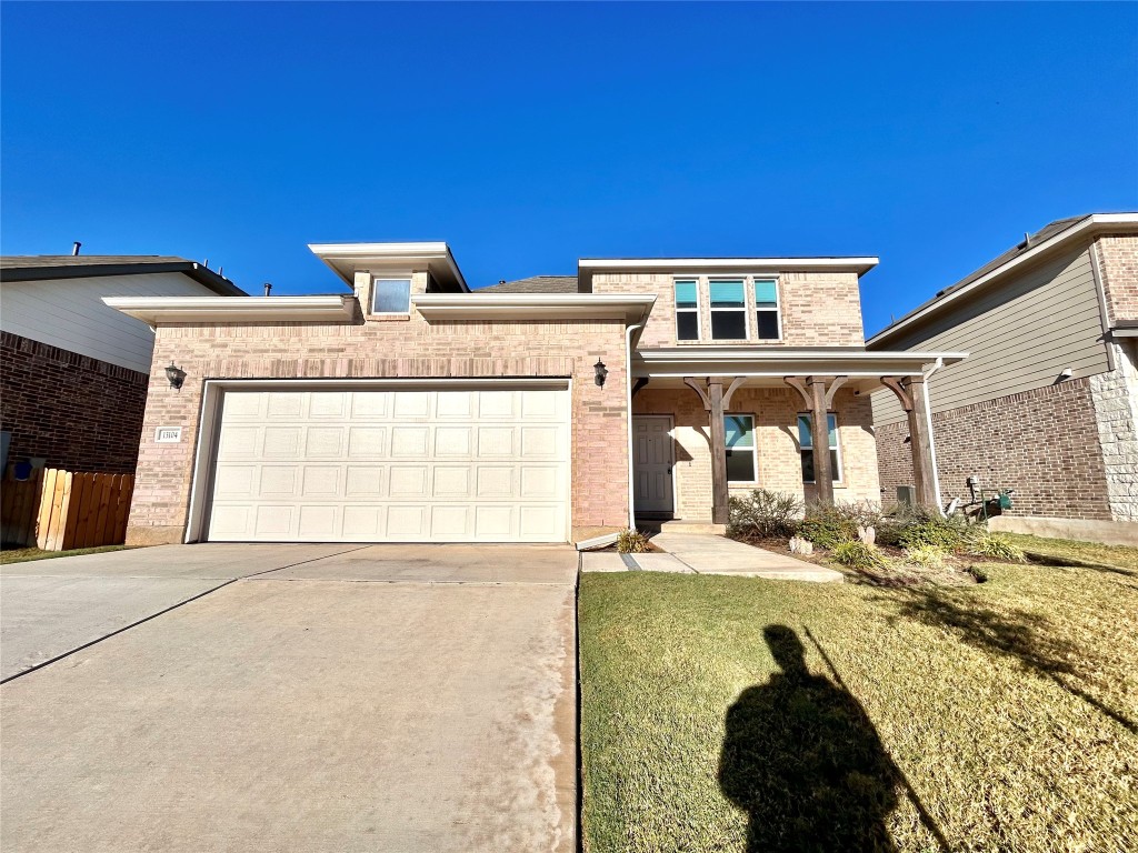 View of front facade featuring brick siding, driveway, covered porch, an attached garage, and a front yard