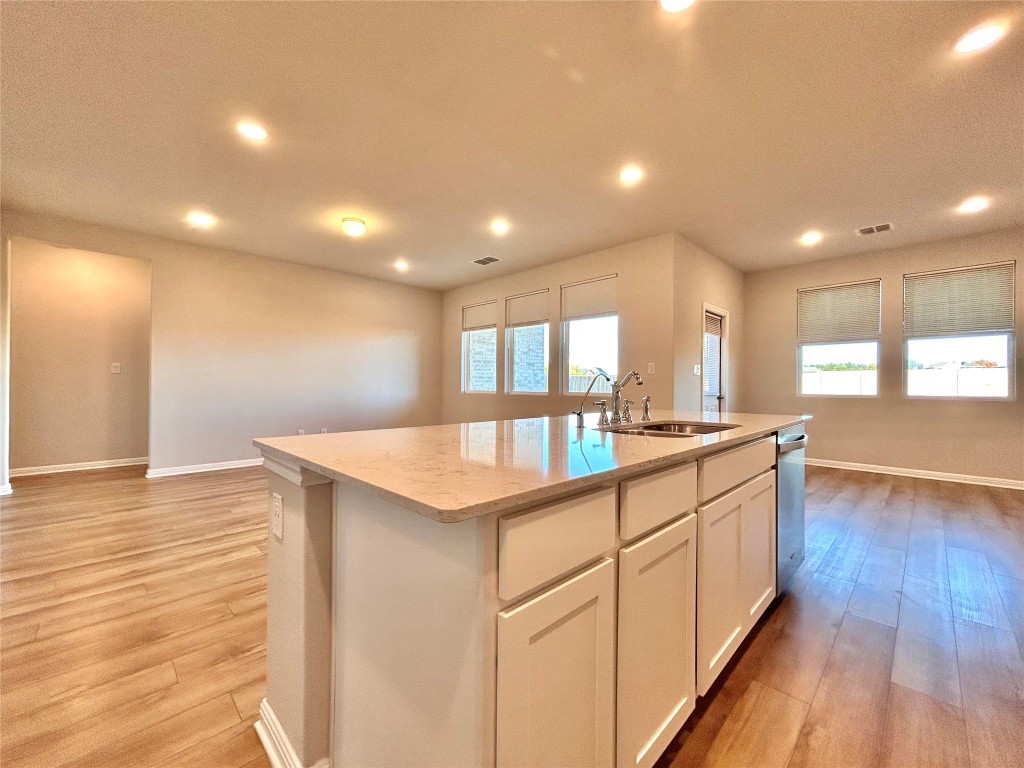 13104 Zumpango Trace Manor, TX 78653 - Photo 10 of 37 Kitchen featuring light stone countertops, white cabinets, light wood-style flooring, recessed lighting, and an island with sink