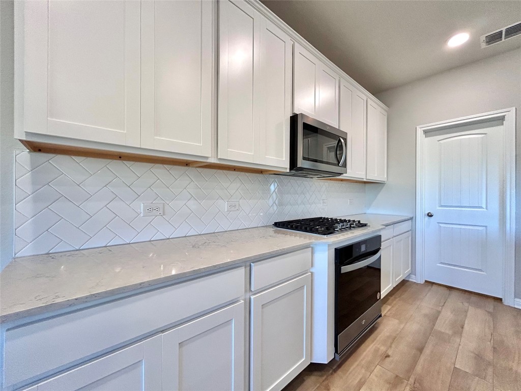 13104 Zumpango Trace Manor, TX 78653 - Photo 8 of 37 Kitchen with light stone countertops, white cabinets, light wood-type flooring, stainless steel appliances, and recessed lighting