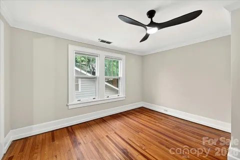 an empty room with wooden floor chandelier fan and windows