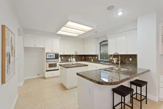 a kitchen with granite countertop a stove a sink and white cabinets with wooden floor