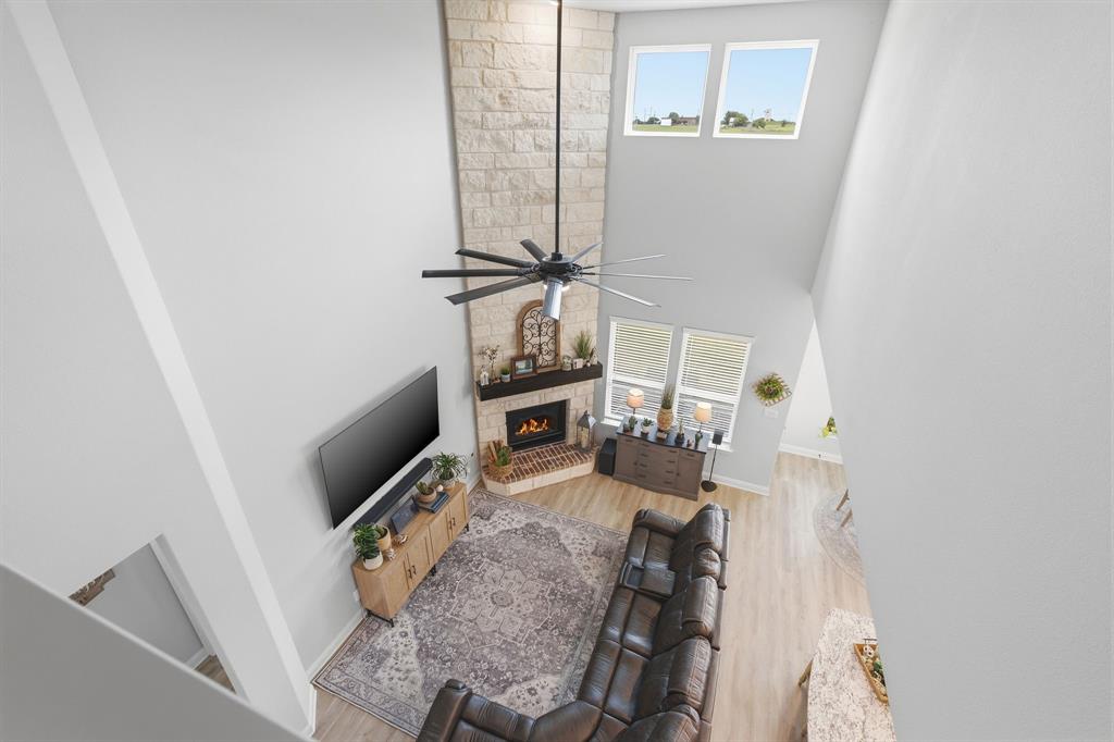 313 Tate Lane Anna, TX 75409 - Photo 19 of 30 Two-story living area featuring a stone-clad fireplace with a dark wood mantel, high vaulted ceilings, and light wood-finish flooring