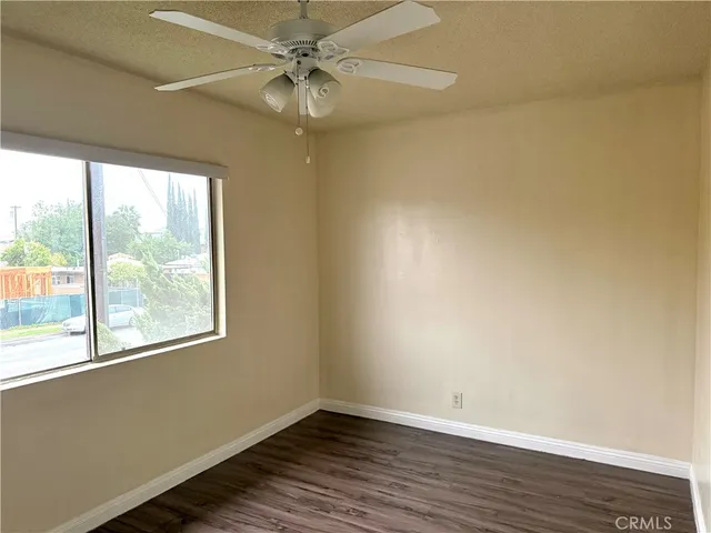 an empty room with wooden floor fan and windows