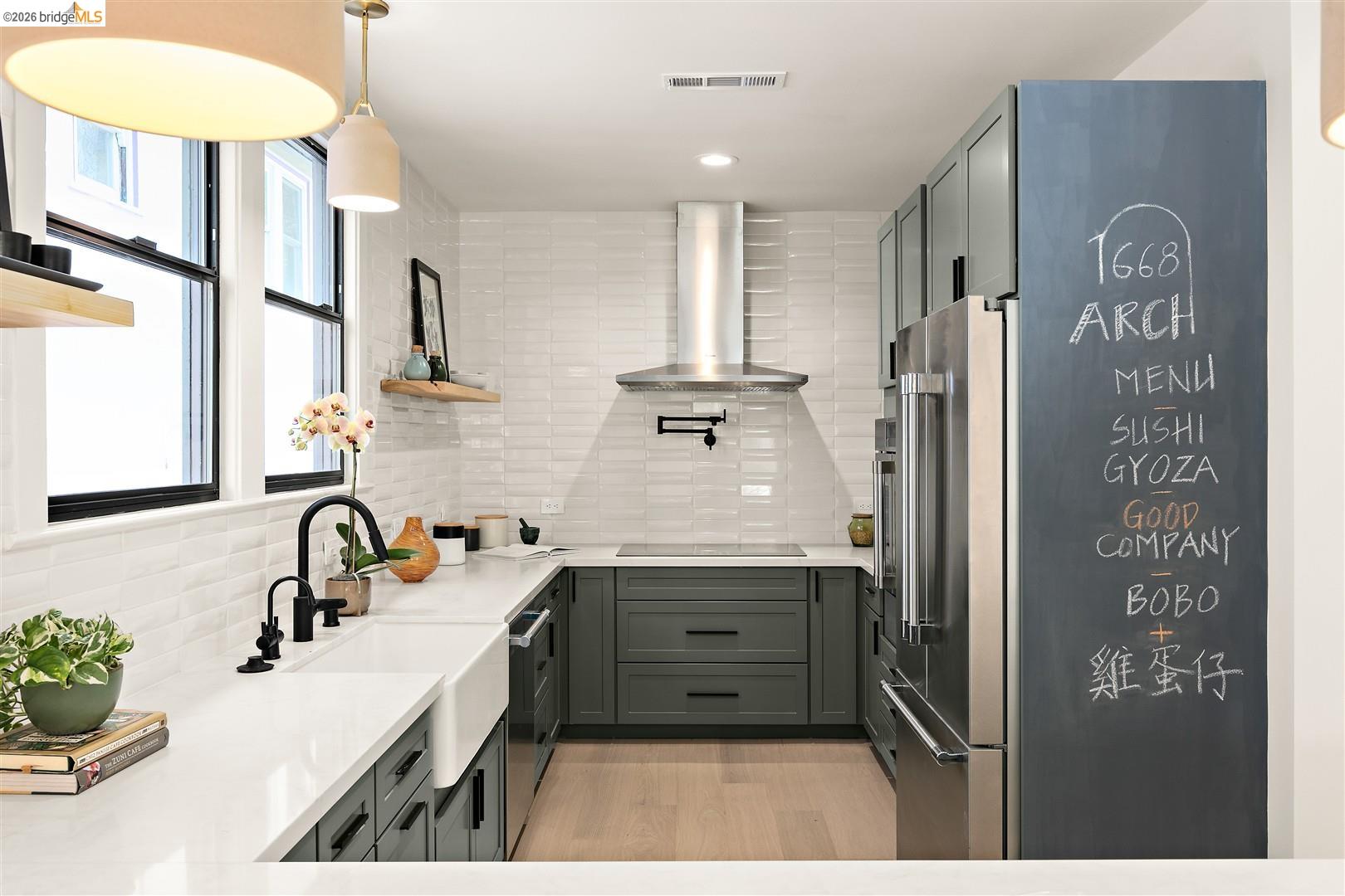 1668 Arch Street Berkeley, CA 94709 - Photo 23 of 78 Contemporary kitchen featuring dark green cabinetry, white subway tile backsplash, stainless steel appliances, a farmhouse sink, and light wood-finish flooring
