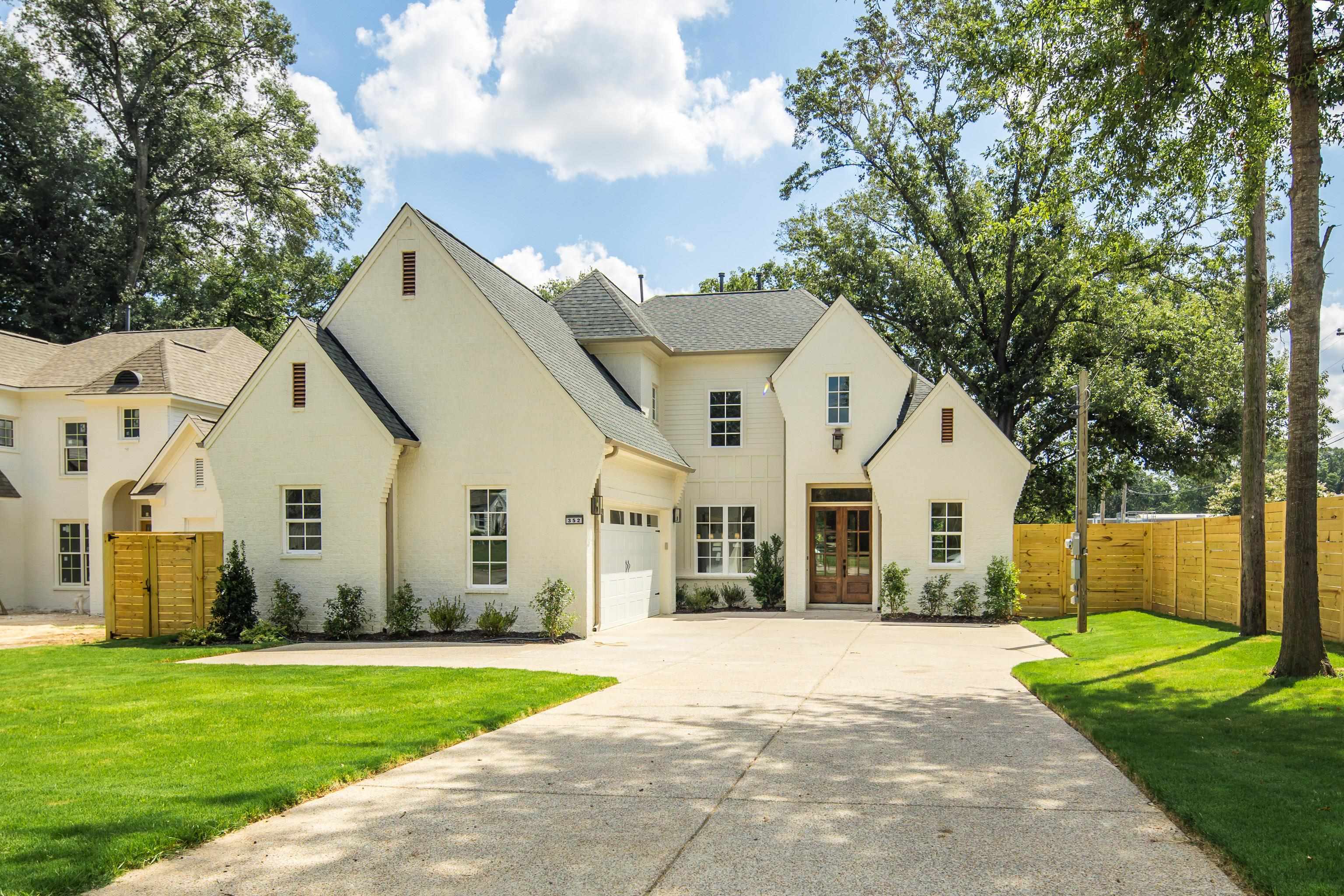 French country home featuring an attached garage, concrete driveway, a shingled roof, french doors, and a gate