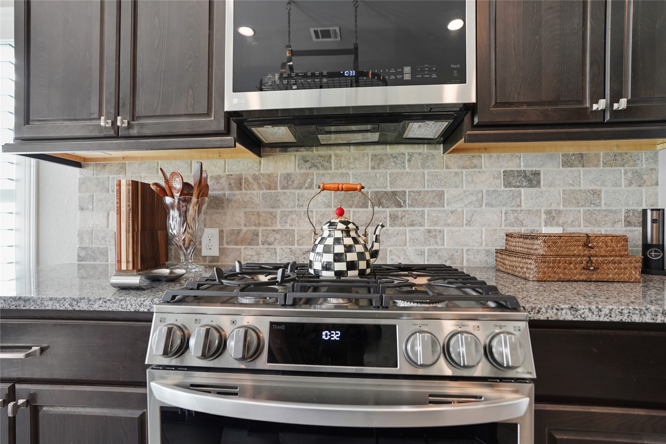 2345 Redwood Ridge Trail Manvel, TX 77578 - Photo 14 of 39 This kitchen features a modern gas stove with a stylish backsplash and dark wood cabinets. The countertop provides ample space, complemented by a decorative checkered teapot and organized utensils.