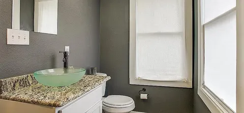 a bathroom with a granite countertop sink a toilet and mirror