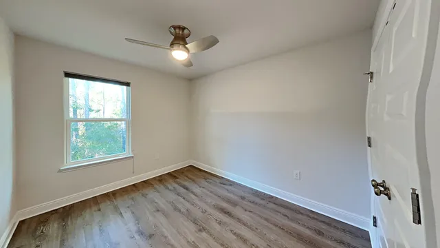 an empty room with wooden floor chandelier fan and windows