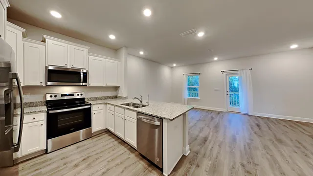 a kitchen with stainless steel appliances granite countertop a stove top oven a sink dishwasher and a microwave with wooden floor
