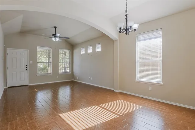 an empty room with wooden floor chandelier and windows