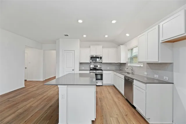 an empty room with wooden floor chandelier fan and windows