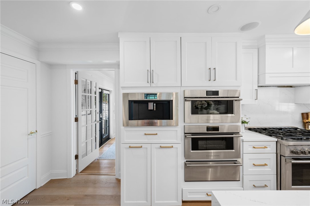 25870 Kennedy Ridge Road North Olmsted, OH 44070 - Photo 21 of 50 Contemporary kitchen featuring white cabinetry, integrated stainless steel appliances, a gas range with a matching hood, and light wood-finish flooring