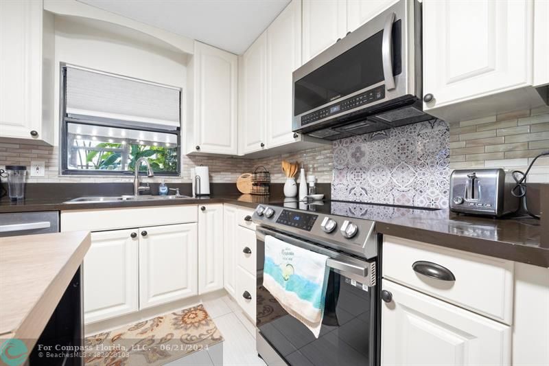 1088 Raintree Drive Palm Beach Gardens, FL 33410 - Photo 9 of 36 a kitchen with stainless steel appliances granite countertop a sink a stove a microwave and wooden cabinets