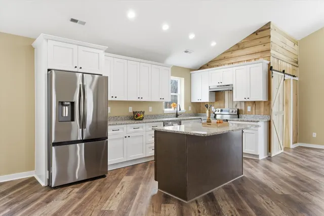 a kitchen with kitchen island a sink a refrigerator a stove and white cabinets