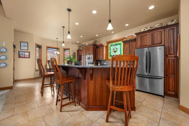 a kitchen with stainless steel appliances granite countertop a refrigerator a sink dishwasher and a dining table with wooden cabinet